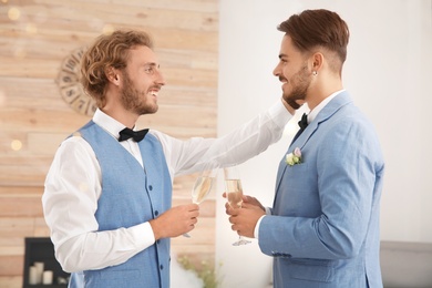 Happy newlywed gay couple with glasses of champagne at home