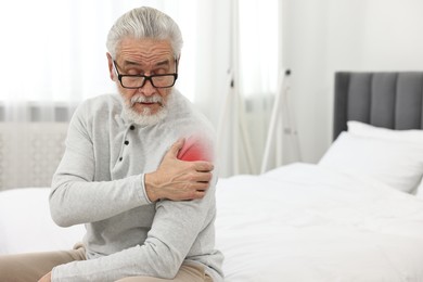 Image of Senior man suffering from pain in shoulder on bed at home. Space for text