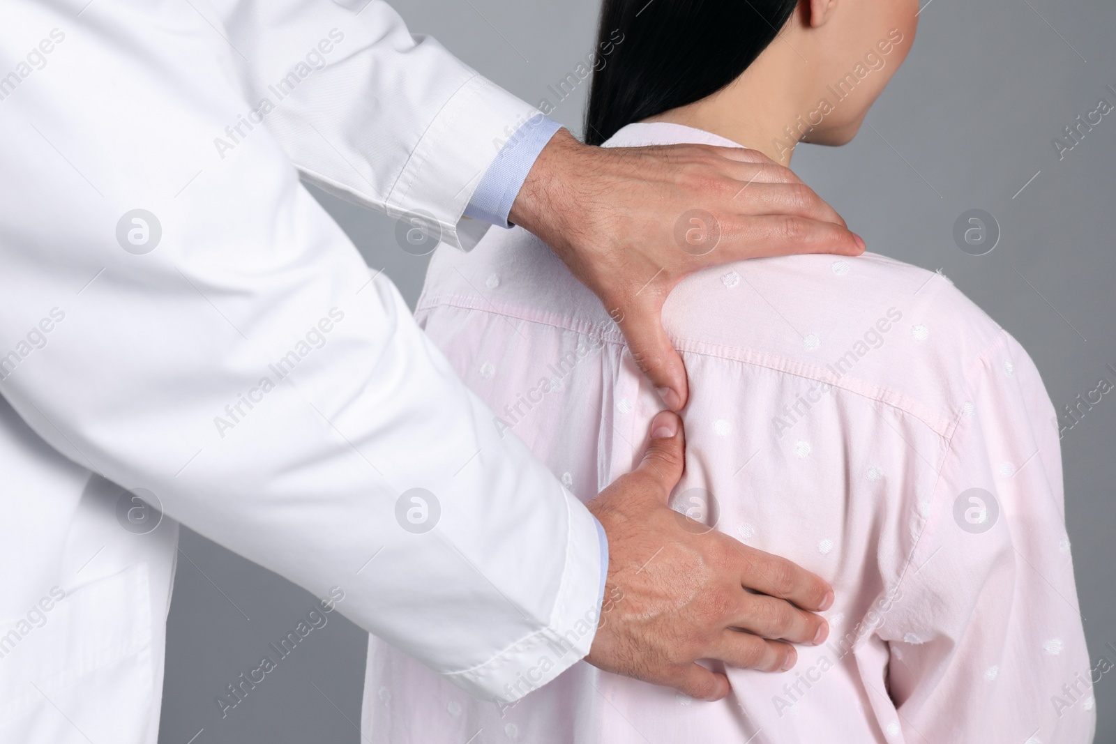 Photo of Doctor examining woman with shoulder pain on grey background, closeup