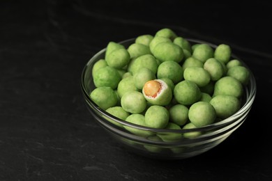 Photo of Tasty wasabi coated peanuts in glass bowl on black table, closeup. Space for text