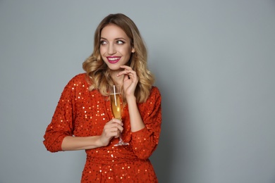 Happy woman in shiny dress with glass of champagne on grey background, space for text. Christmas party
