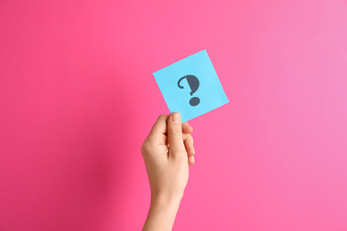 Woman holding note with question mark on pink background, closeup