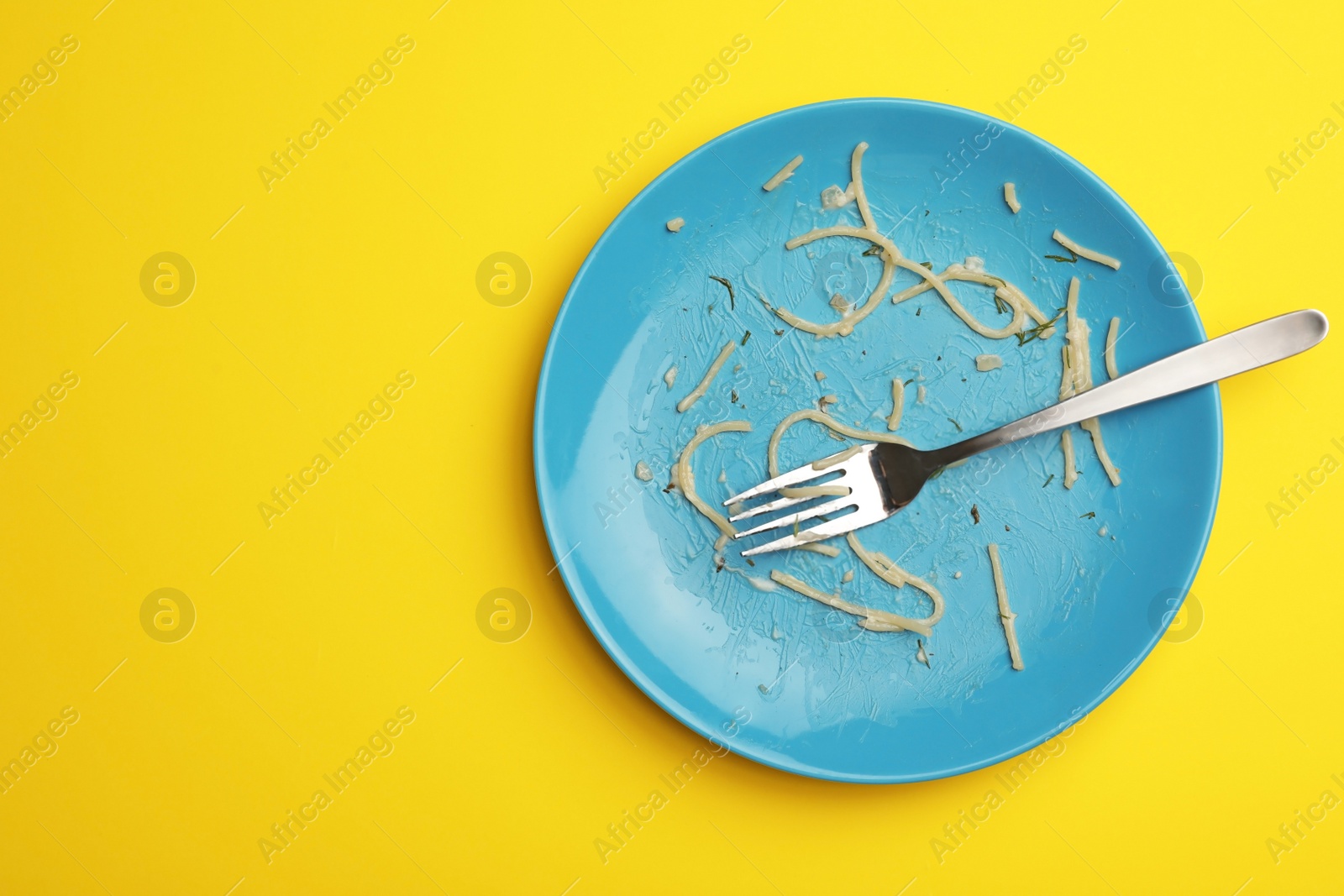 Photo of Dirty plate with food leftovers and fork on yellow background, top view. Space for text