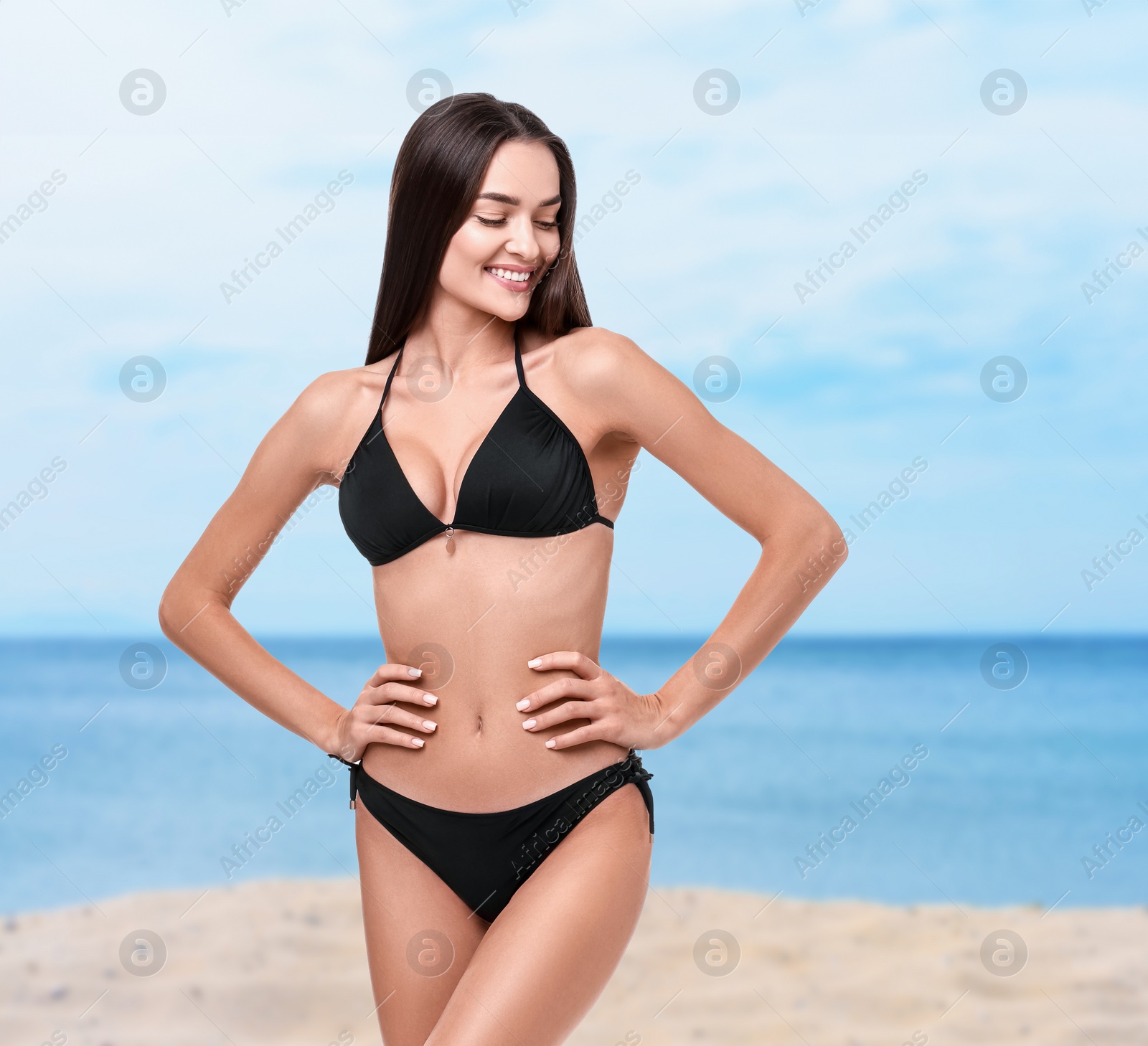 Image of Happy woman in stylish black bikini on sandy beach near sea