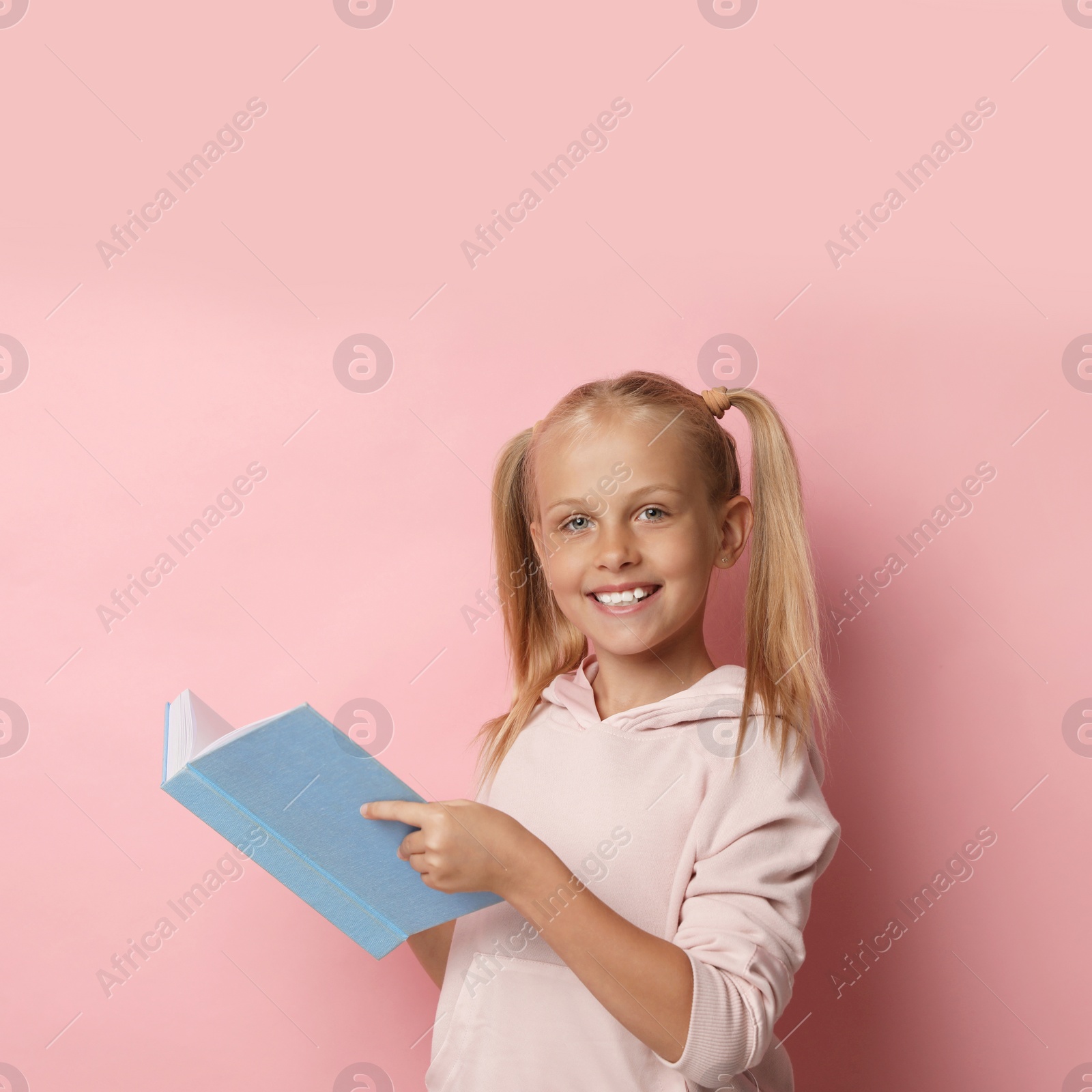 Photo of Portrait of cute little girl reading book on pink background