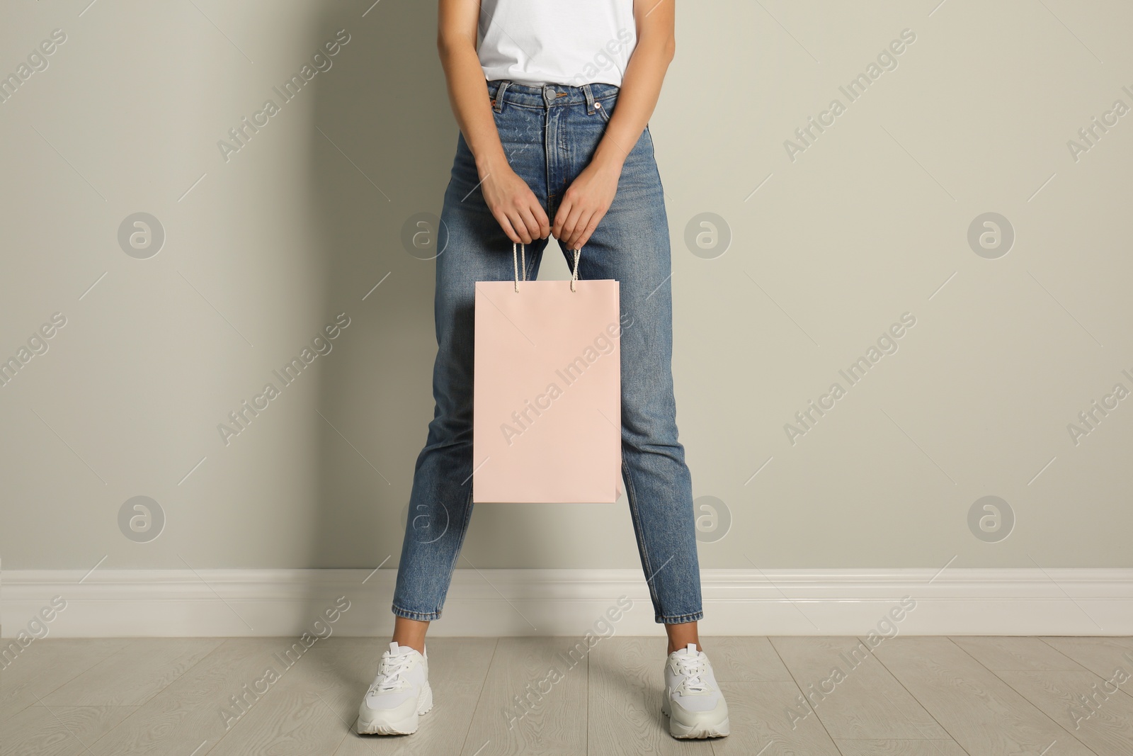 Photo of Woman with paper shopping bag near light grey wall, closeup