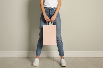 Photo of Woman with paper shopping bag near light grey wall, closeup