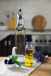 Photo of Different cooking oils, olives, basil and lavender flowers on wooden table in kitchen
