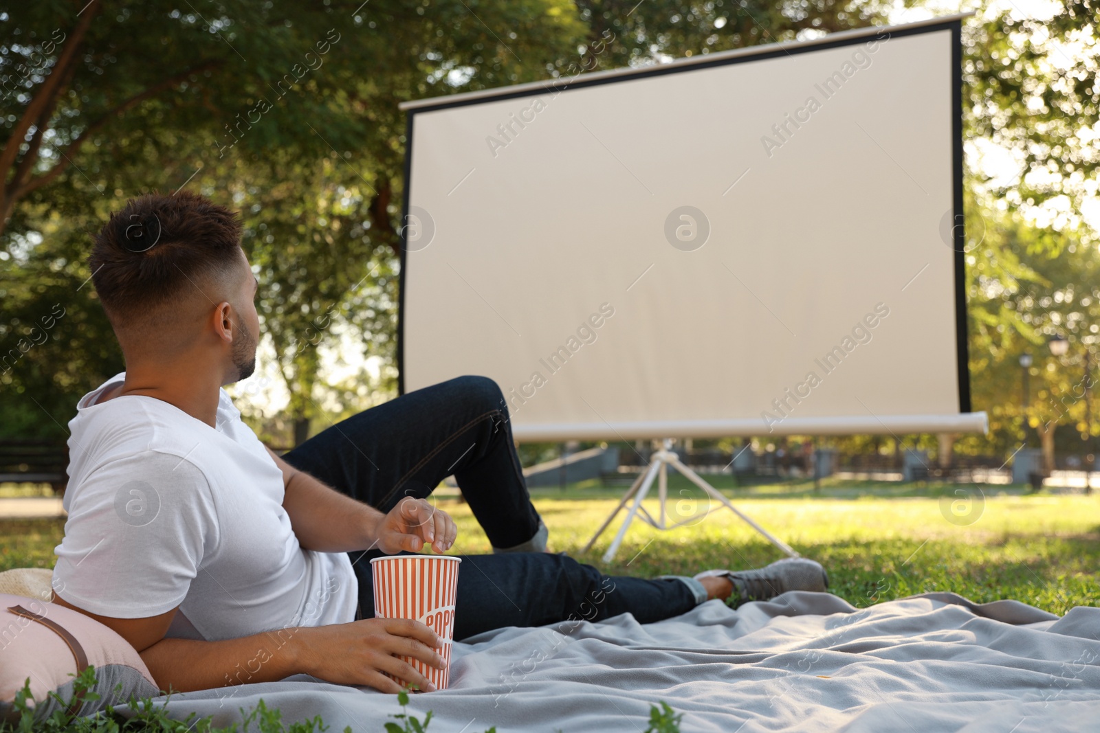 Photo of Young man with popcorn watching movie in open air cinema. Space for text