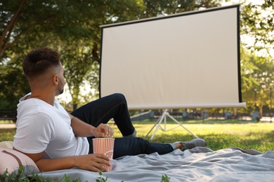 Young man with popcorn watching movie in open air cinema. Space for text