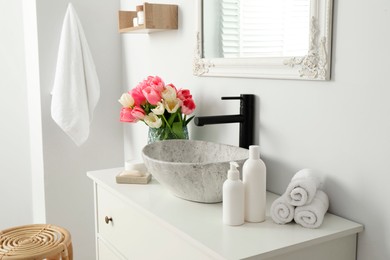 Photo of Vase with beautiful pink tulips and toiletries near sink in bathroom