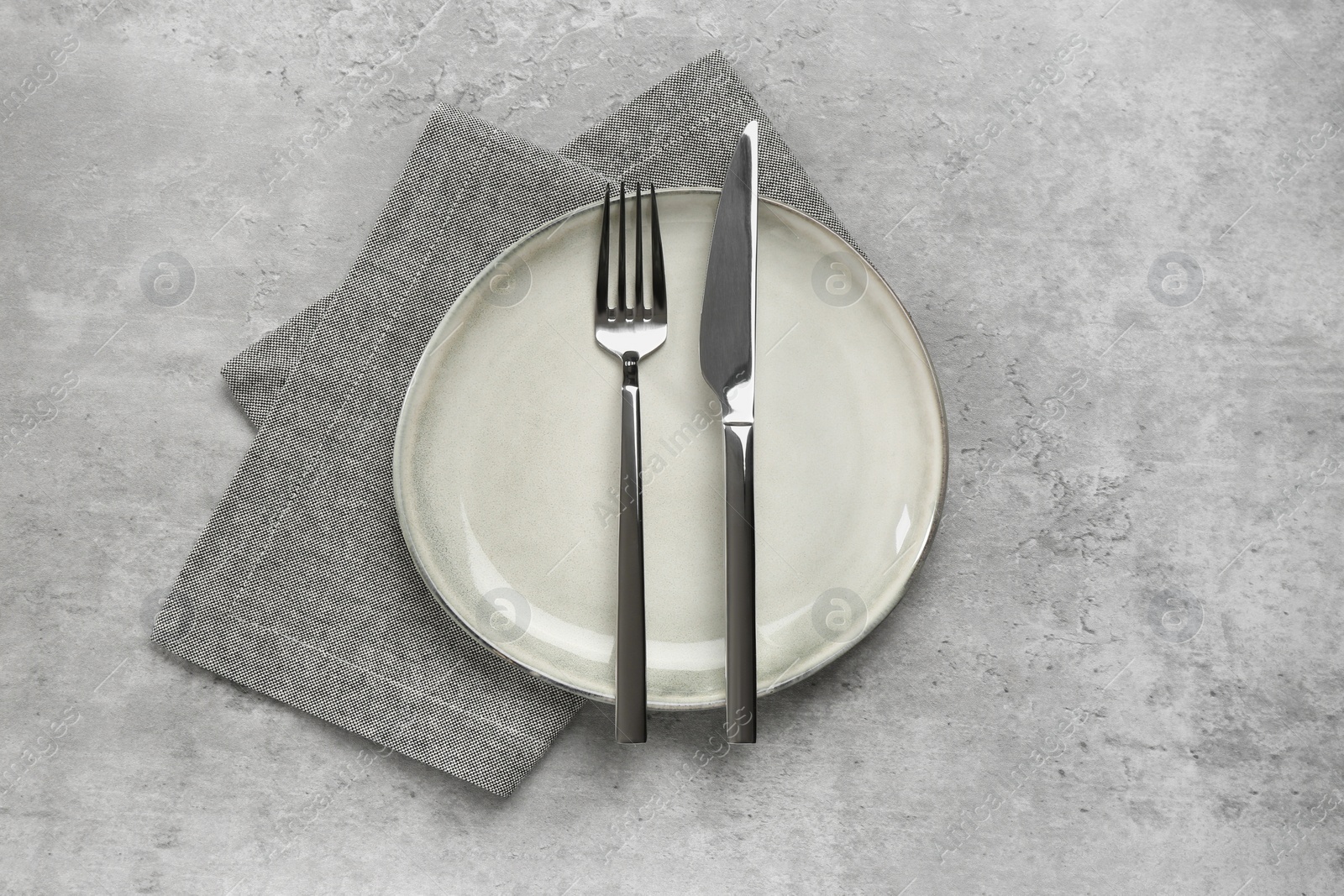 Photo of Clean plate with shiny silver cutlery on light grey table, flat lay