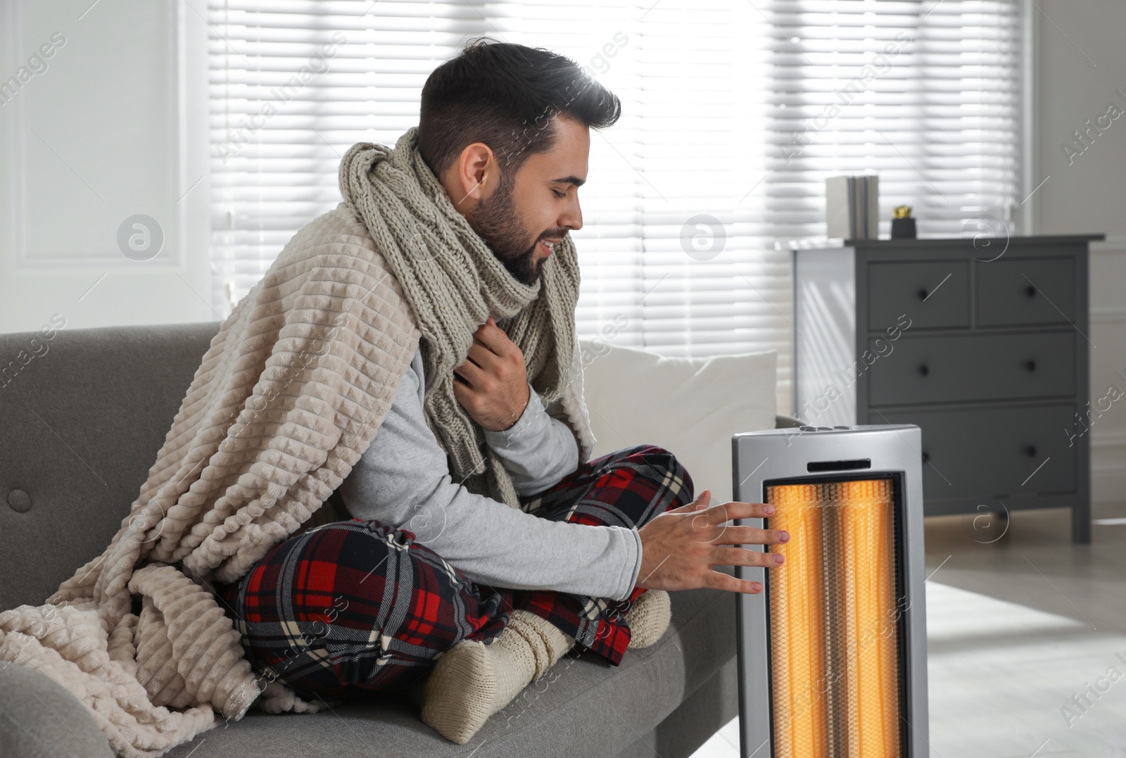 Photo of Young man getting warm near electric heater at home