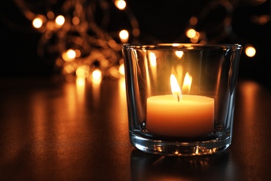 Photo of Wax candle burning on table in darkness, closeup