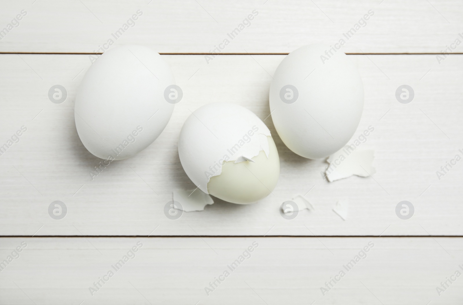 Photo of Boiled eggs and pieces of shell on white wooden table, flat lay