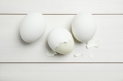 Boiled eggs and pieces of shell on white wooden table, flat lay