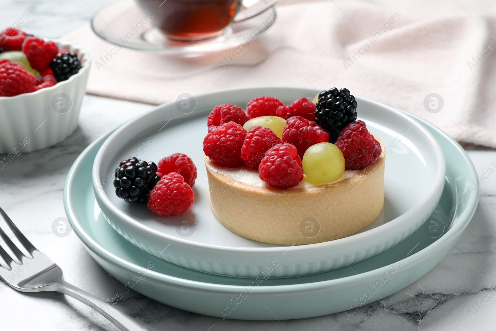 Photo of Delicious tartlet with berries on white marble table