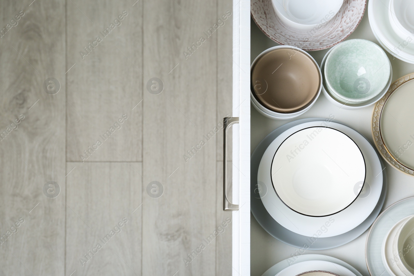 Photo of Open drawer with different plates and bowls in kitchen, top view. Space for text