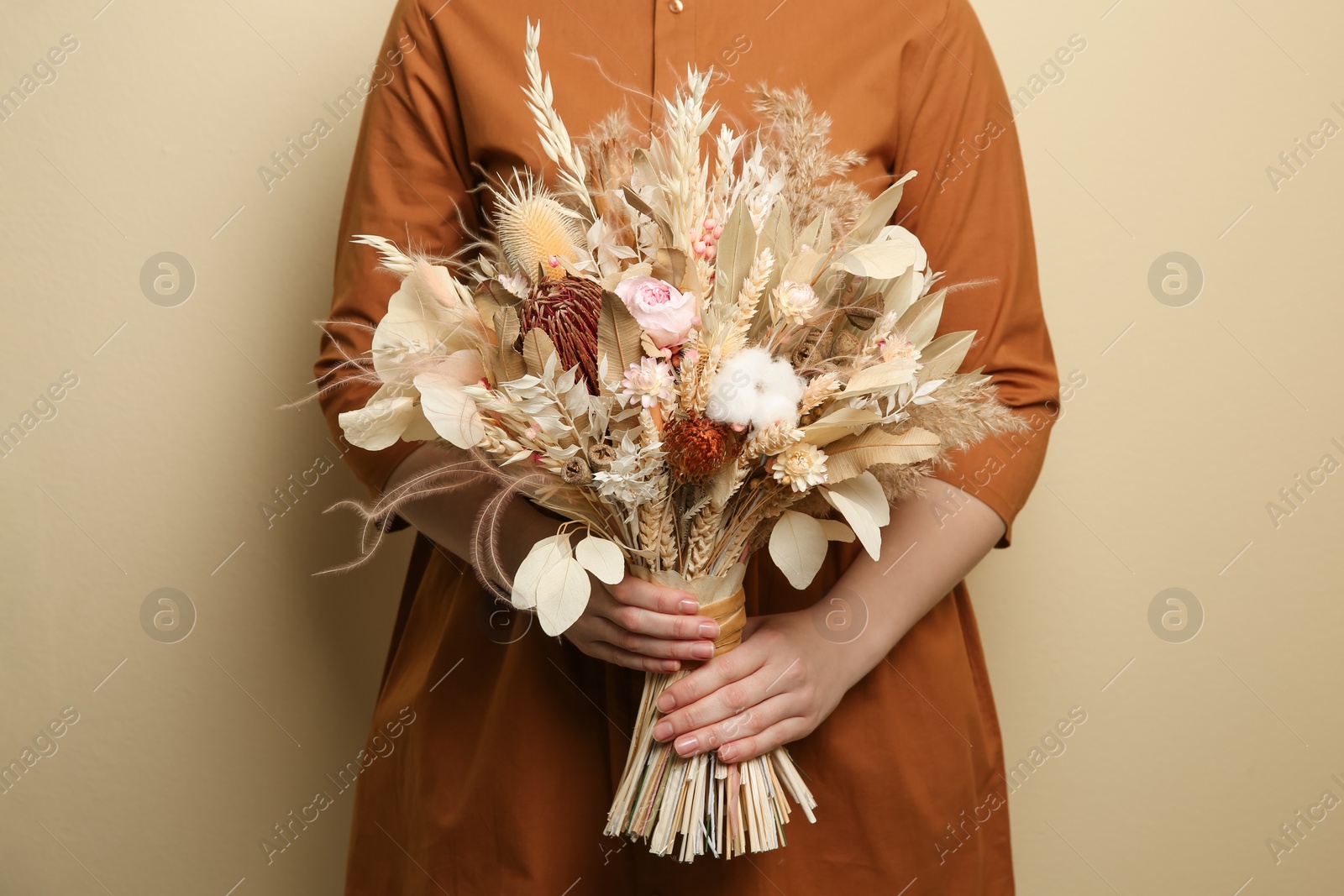 Photo of Woman holding beautiful dried flower bouquet on beige background, closeup