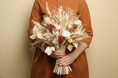 Woman holding beautiful dried flower bouquet on beige background, closeup
