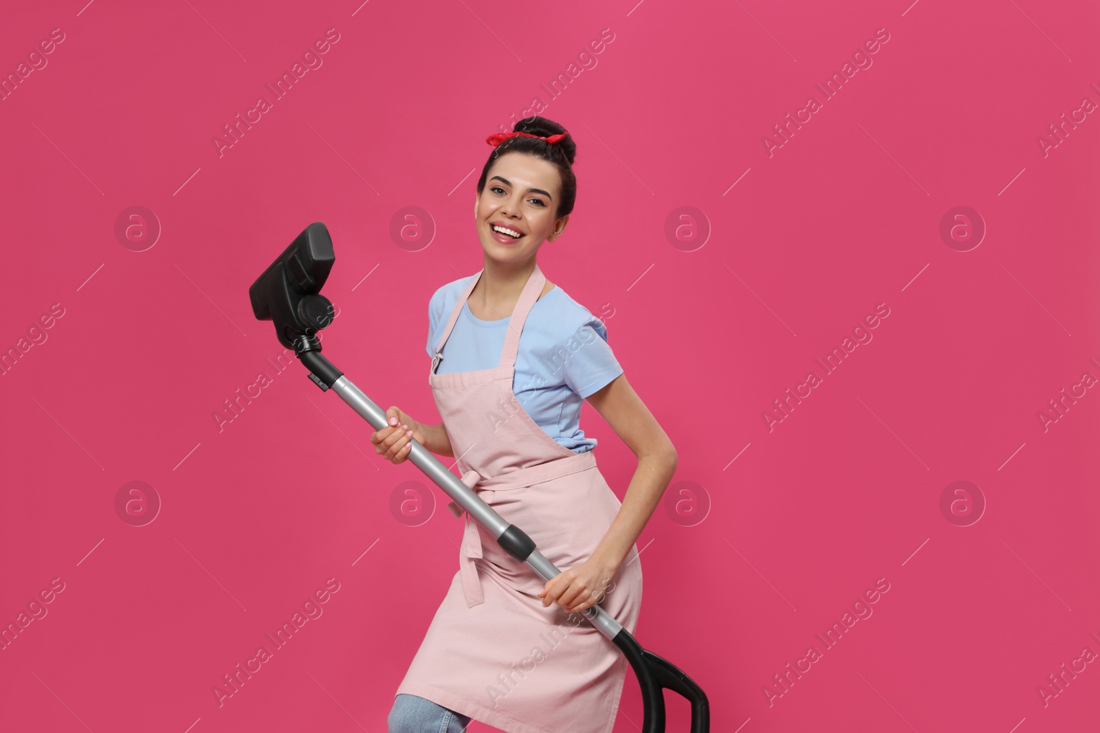 Photo of Housewife with vacuum cleaner on pink background