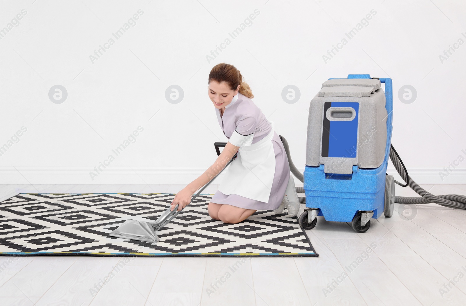 Photo of Female worker removing dirt from carpet with professional vacuum cleaner indoors