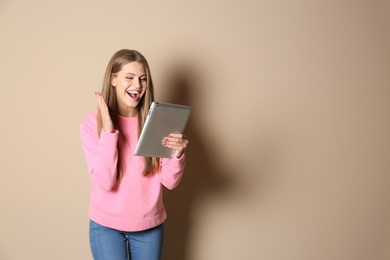 Emotional young woman with tablet celebrating victory on color background. Space for text