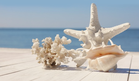 Beautiful starfish, coral and shell on wooden pier near sea, closeup