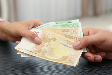 People with Euro banknotes at table indoors, closeup
