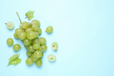 Photo of Bunch of ripe grapes with green leaves on light blue background, flat lay. Space for text