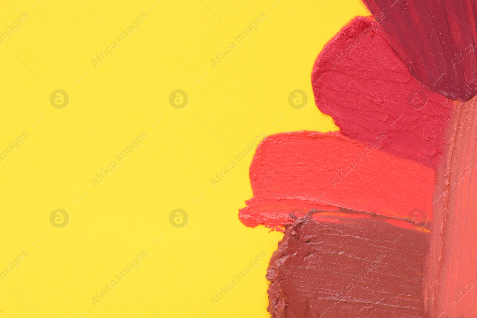 Photo of Smears of different beautiful lipsticks on yellow background, top view. Space for text