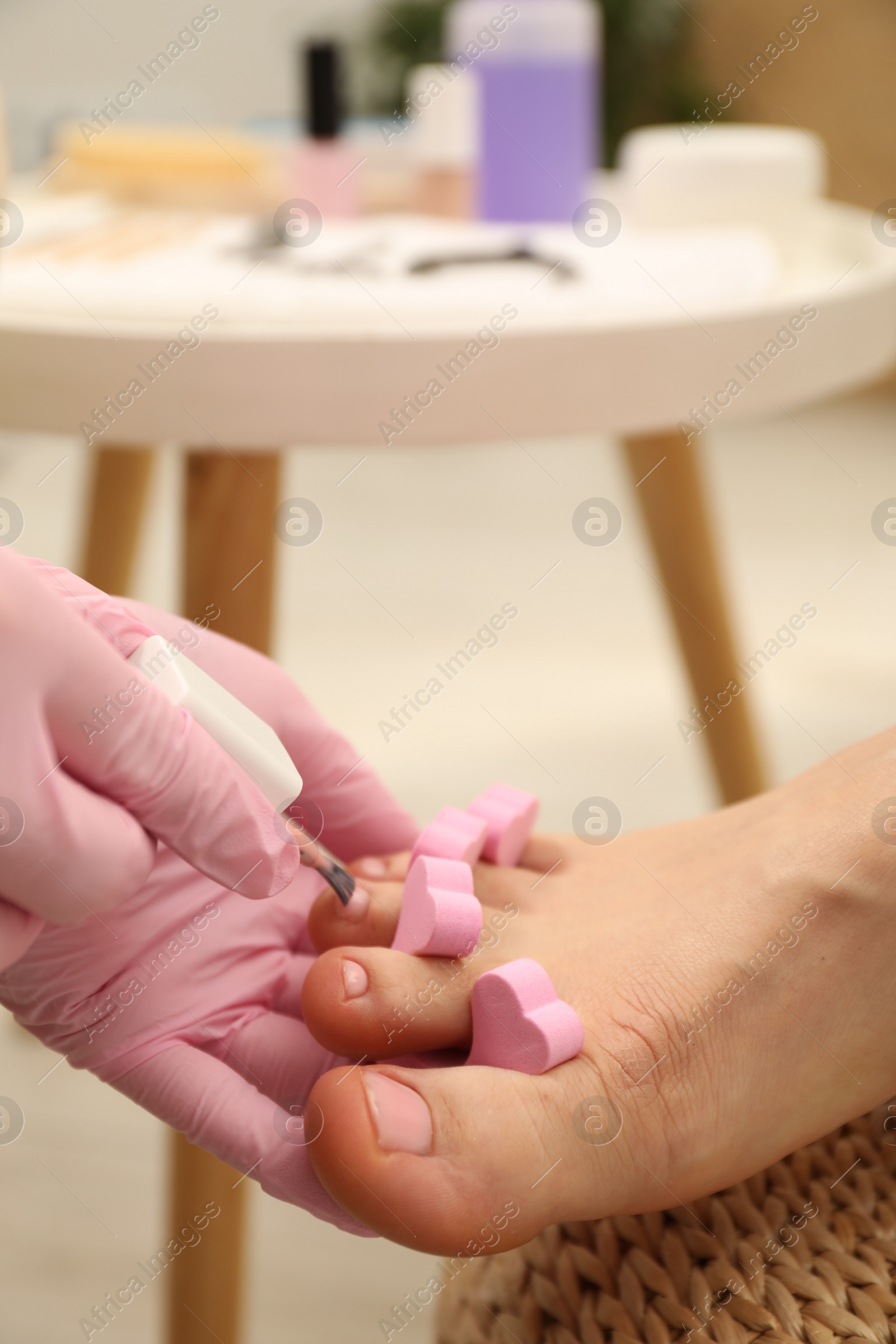 Photo of Professional pedicurist painting client`s toenails with polish in beauty salon, closeup