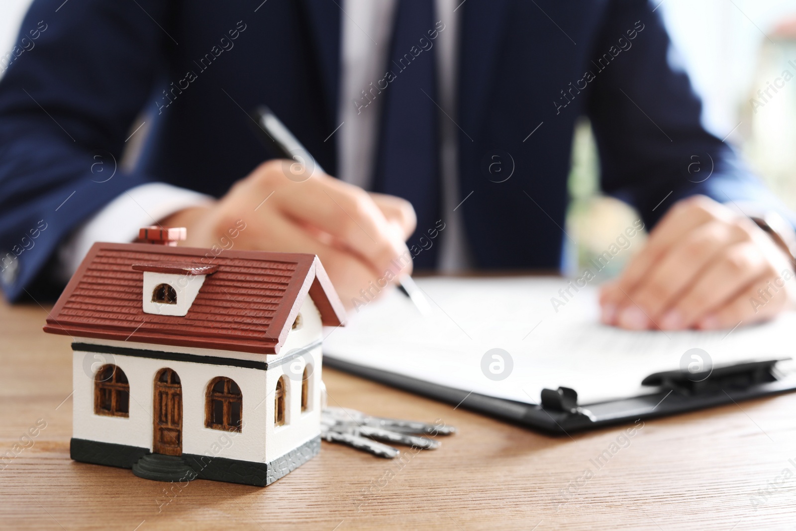 Photo of House model and blurred real estate agent on background, closeup