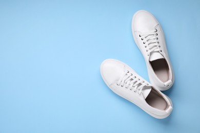 Photo of Pair of stylish white sneakers on light blue background, top view. Space for text