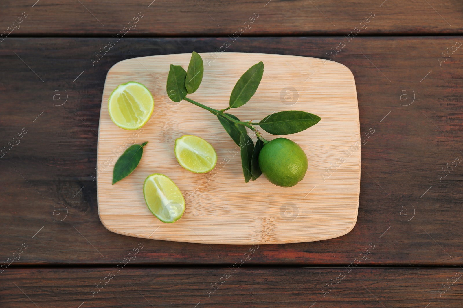 Photo of Board with fresh limes and leaves on wooden table, top view