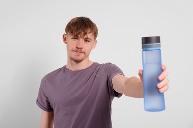 Man holding transparent plastic bottle with drink on light grey background