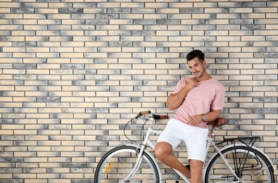 Handsome young hipster man with bicycle on brick wall background