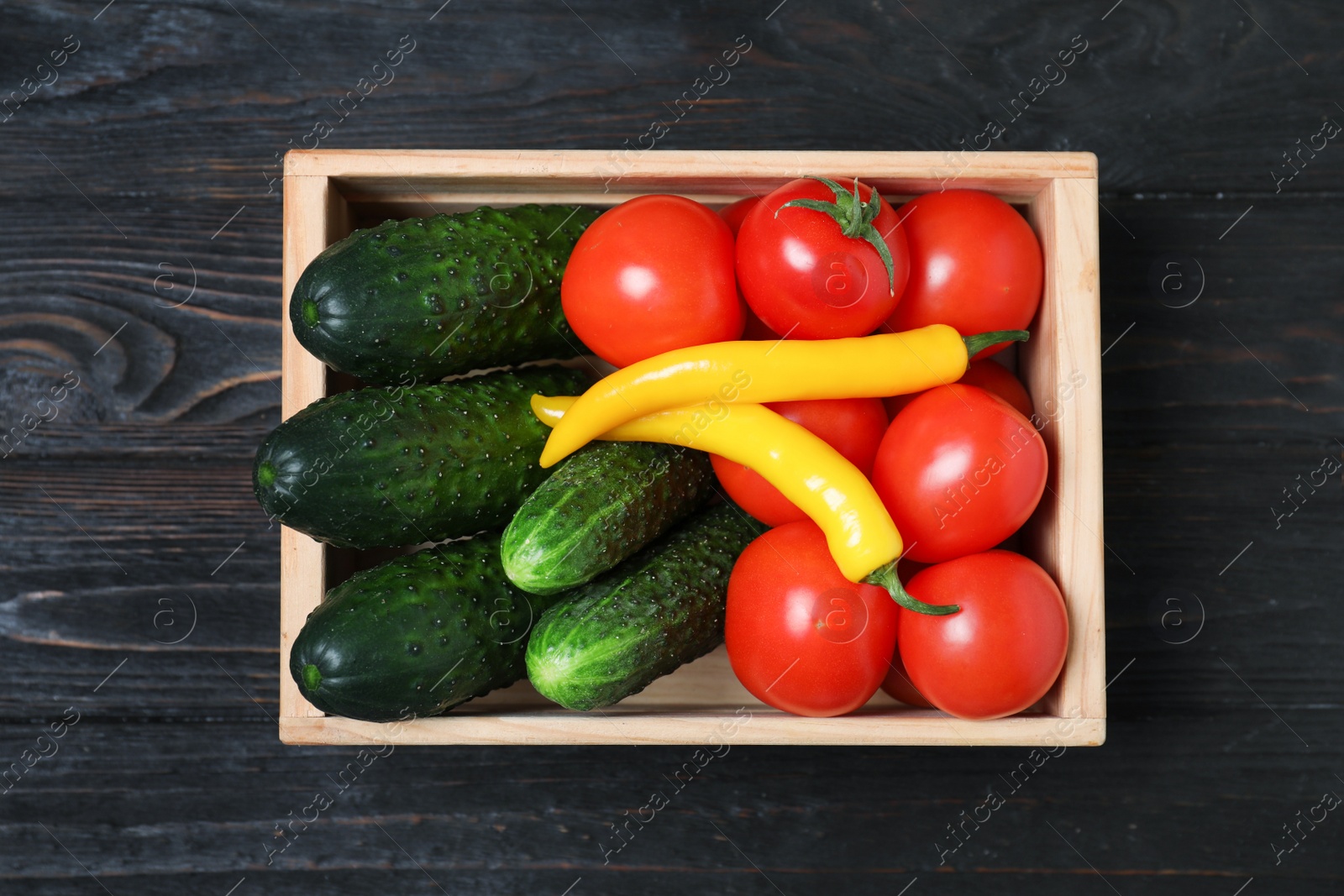 Photo of Wooden crate full of fresh vegetables on dark background, top view