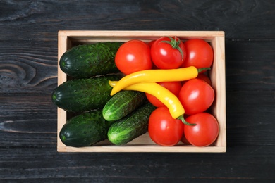 Wooden crate full of fresh vegetables on dark background, top view