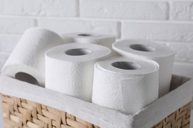 Toilet paper rolls in wicker basket near white brick wall, closeup