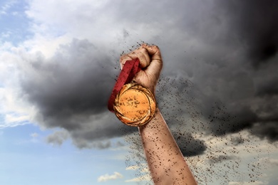 Image of Winner raising hand with gold medal through dirt up to sky, closeup