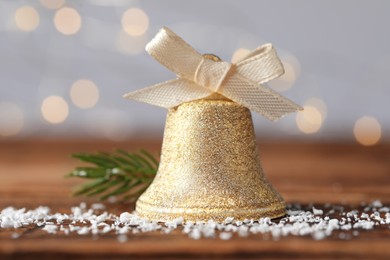 Photo of Bell with bow and artificial snow on table against blurred background, closeup. Christmas decor