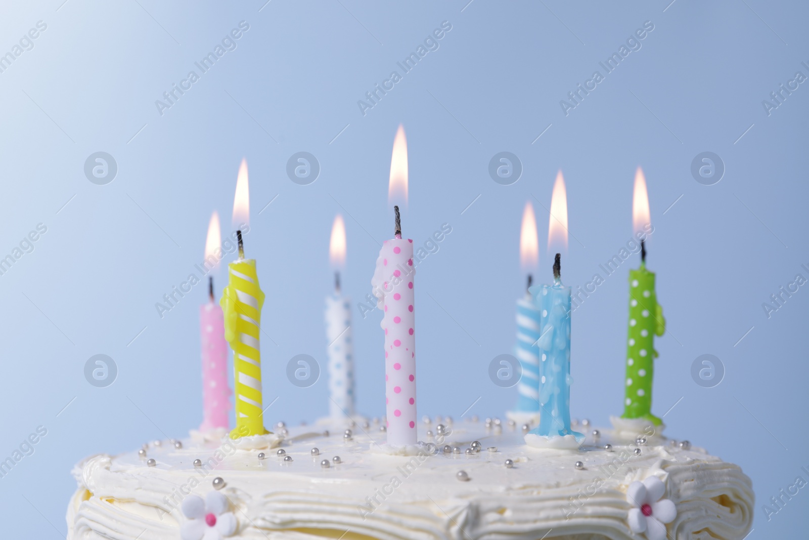 Photo of Delicious cake with cream and burning candles on light blue background, closeup