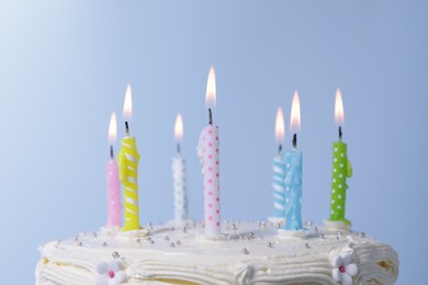 Photo of Delicious cake with cream and burning candles on light blue background, closeup