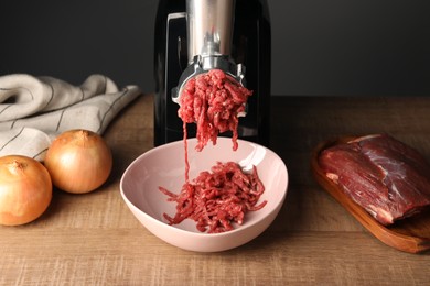 Photo of Electric meat grinder with beef mince and onion on wooden table