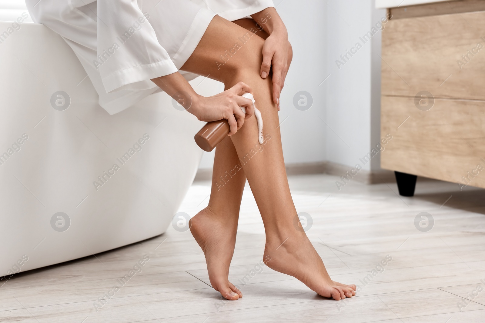 Photo of Woman applying self-tanning product onto her leg on tub in bathroom, closeup