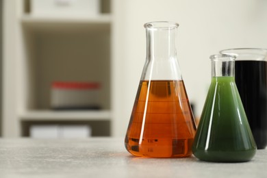 Photo of Flasks and beaker with different types of crude oil on light grey table, space for text