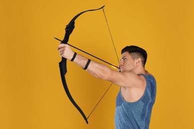 Photo of Man with bow and arrow practicing archery on yellow background