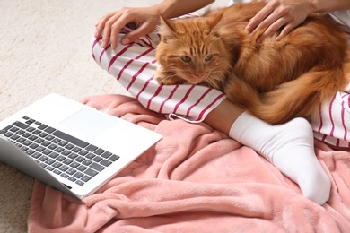 Woman with cute red cat and laptop on carpet at home, closeup view