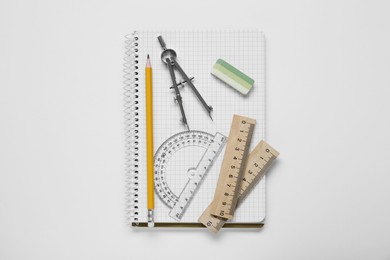 Photo of Protractor ruler, compass, pencil and notebook on white background, top view